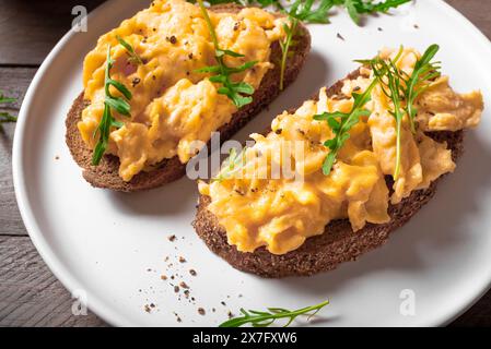 Scrambled Eggs Sandwiches for healthy keto breakfast. Whole grain toasts with scramble eggs and organic arugula microgreens on white plate close up. Stock Photo