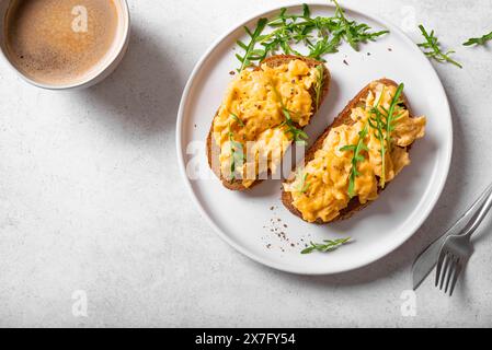 Scrambled Eggs Sandwiches and coffee for healthy keto breakfast. Whole grain toasts with scramble eggs and organic arugula microgreens on white table, Stock Photo