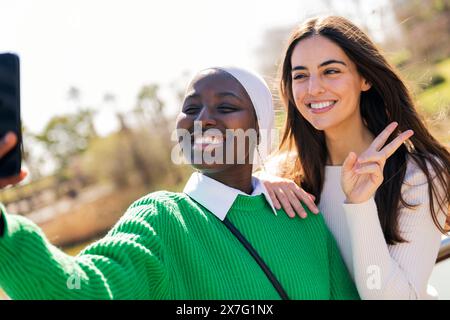 two young female friends smiling happy while taking selfie photo with mobile phone, concept of friendship and modern lifestyle Stock Photo