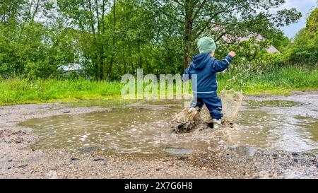 The child runs through puddles in rubber boots and a waterproof suit ...