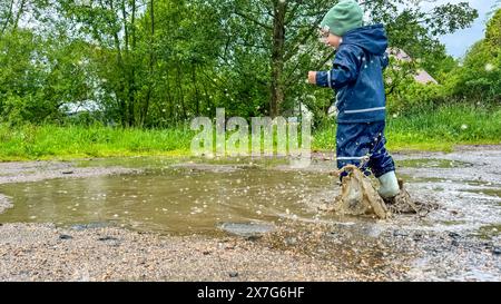 The child runs through puddles in rubber boots and a waterproof suit ...