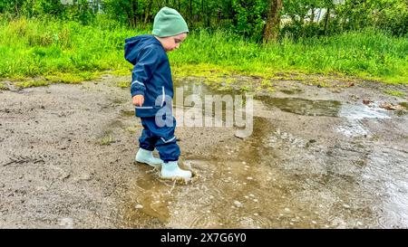 The child runs through puddles in rubber boots and a waterproof suit ...