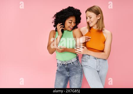 Two diverse women in casual attire standing on a pink background. Stock Photo