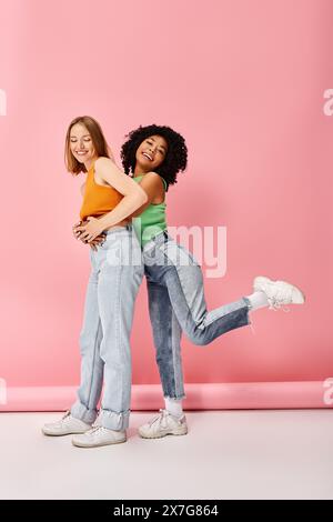 Two young women in casual attire hug in front of a pink wall. Stock Photo