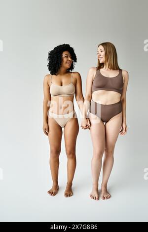 Two diverse women in cozy pastel bikinis standing together. Stock Photo