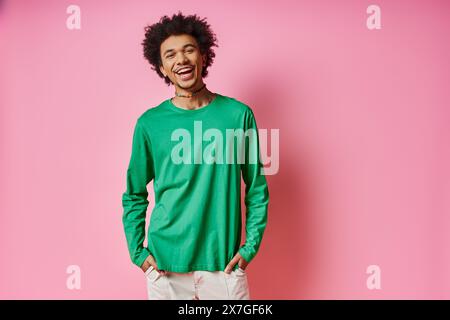 A cheerful young African American man in casual wear stands in front of a pink wall, showcasing his emotions. Stock Photo