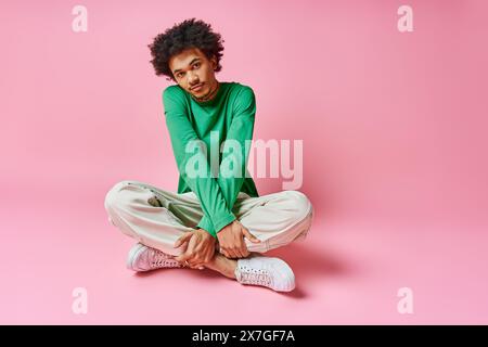 A cheerful young African American man with curly hair sits cross-legged on the ground, deep in thought. Stock Photo