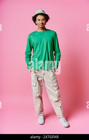 A cheerful young African American man with curly hair wearing casual green shirt and khaki pants against a pink background. Stock Photo
