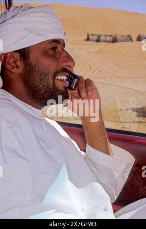 Wahiba Sands, Oman, Arabian Peninsula, Middle East - Bedouin Driver Using Cell Phone. Stock Photo