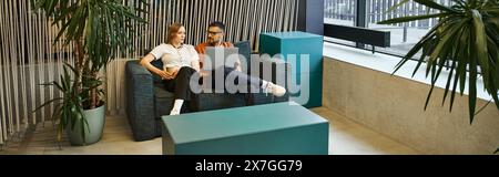Two coworkers relax and chat on a couch in a modern workspace, reflecting a startup teams dynamic lifestyle. Stock Photo