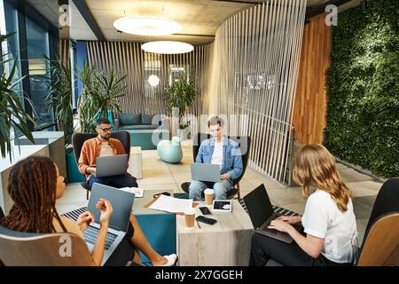 A diverse group of professionals sit around a table, engrossed in their laptops, collaborating on a startup project. Stock Photo