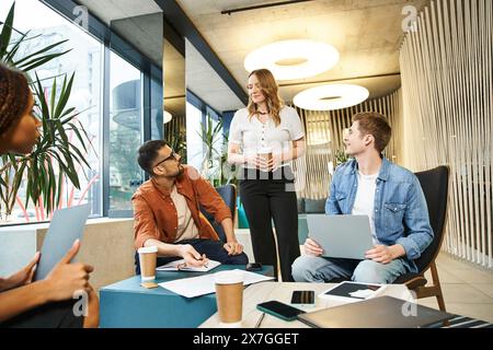 A diverse group of individuals sit around a table, laptops open, collaborating on projects in a coworking space. Stock Photo