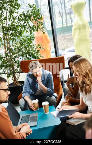 Multicultural colleagues collaborating at a table, immersed in work on their laptop during a corporate trip in a hotel lobby. Stock Photo