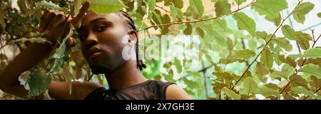 A handsome African American man with dreadlocks stands confidently in front of a vibrant tree. Stock Photo