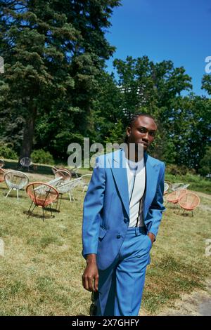 Stylish African American man in blue suit standing in vibrant green place. Stock Photo