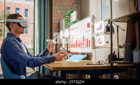 Successful Young Man Sitting in Loft Living Room, Using Virtual Reality Headset with Controllers to Work From Home on Business Financial Reports. Manager Using Office Software for Analyzing Expenses. Stock Photo