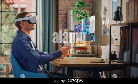 Excited Young Man Sitting in Loft Living Room at Home, Using Virtual Reality Headset with Controllers to Check Social Media Streaming Application. Male Choosing to Watch Life in Space Documentary. Stock Photo