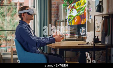 Handsome Young Man Sitting in Loft Living Room at Home, Using Virtual Reality Headset with Controllers to Check Social Media Streaming Application. Male is Watching a Cooking TV Show. Stock Photo