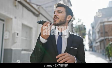 Handsome hispanic man in suit sends voice message on city street Stock Photo