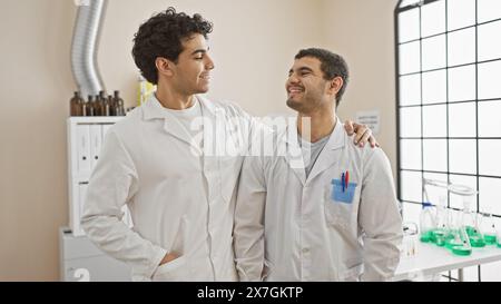 Two men in white lab coats bonding and smiling in a well-equipped modern laboratory. Stock Photo