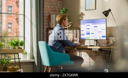 Remote Work Concept: Man Using Desktop Computer With Office Software to Check Schedule in Calendar. Young Male Planning Business Meetings in Stylish Loft Apartment with Big Window. Stock Photo