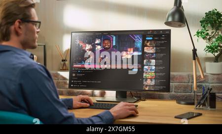 Handsome Man Watching Video Sharing Service Mock-up Where African American Influencer Talks About Lifestyle. Celebrity Blogger Having fun. Interface with Related Streams, Likes, Comments. Stock Photo