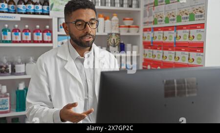 An attentive young black man wearing a lab coat in an indoor pharmacy setting, working on a computer. Stock Photo