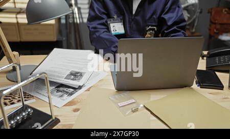 An african american male detective analyzes evidence in a police station office with a laptop and documents on the desk. Stock Photo