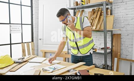Handsome hispanic man using phone while working in a bright carpentry workshop Stock Photo