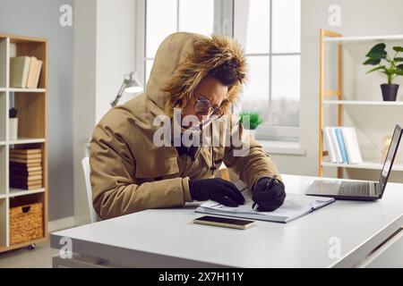 Young indian business man working in the cold at home on his laptop and writing. Stock Photo