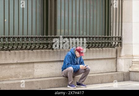 a man sitting on a step on a manhattan sidewalk reading his phone Stock Photo