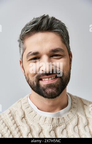 A serene, grey-haired man with a beard, wearing a white sweater, smiles warmly against a grey studio backdrop. Stock Photo