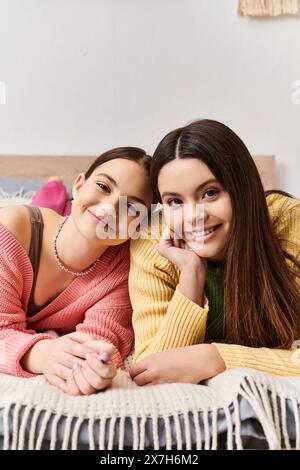 Two beautiful teenage girls in casual clothes lounging together on a bed, enjoying each others company in a cozy setting. Stock Photo