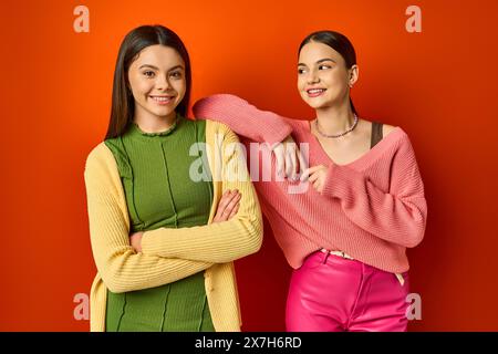 Two pretty, casually dressed brunette teenage girls standing next to each other in front of a vibrant red wall. Stock Photo