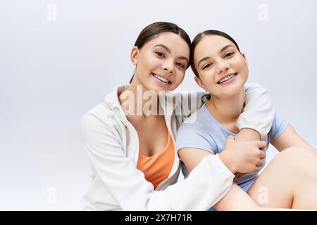 Two pretty, sporty, and brunette teenage girls sitting together in stylish attire on a white background. Stock Photo