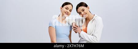 A pair of pretty brunette teenage girls in sporty attire stand next to each other on a grey studio background. Stock Photo