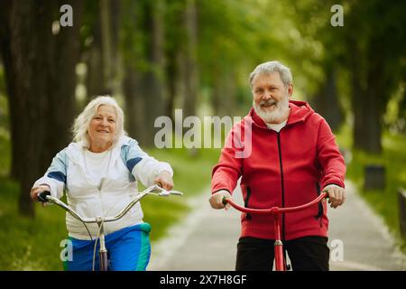 Elderly couple, happy, smiling man and woman enjoying leisurely bicycle ride, staying active, training on early morning. Stock Photo