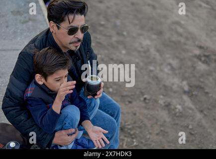 portrait of argentinian son and father sitting in embrace drinking yerba mate outdoors. Latin boy and man Stock Photo