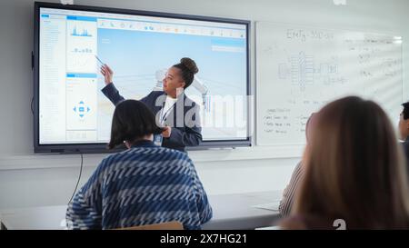Black Female Teacher Explains Principles of Work With Robotic Arm to Group of Students on Seminar. Specialists Working on Autonomous Facility Optimisation. Robotic Engineering and Science Concept. Stock Photo