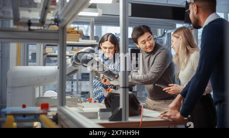 Young Specialists Examine Details of Robotic Hand and Smile During Discussion. Engineers Try to Make Jobs Safer, Easier and More Efficient. Professionals Work on Autonomous Facility Optimisation. Stock Photo