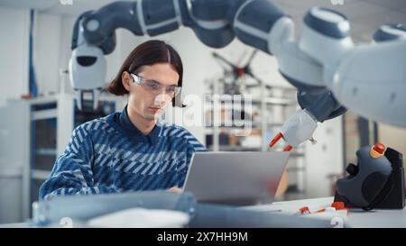 Male Developer Programming Robotic Arm on Laptop. Robotics Engineer Creates Designs by Using 3D, CAD Software. Breakthrough Projects and Computer Science Higher Education Concept. Stock Photo
