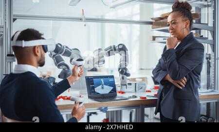 Black Senior Engineer Look at Laptop and Supervising her Young Colleague with VR Headset and Controllers. Virtual Reality Technology for Design, Development and Prototyping in CAD Software. Stock Photo