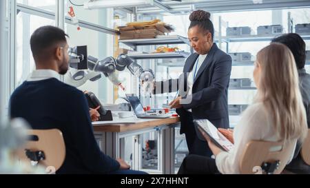 Multi-Ethnic Office, Conference Room. Female Developer does Presentation for Group of Scientists, Uses Laptop, Shows Robot Limb. Businesspeople Brainstorm Strategy in Robotics Technologies. Stock Photo