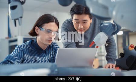 Two Diverse Developers Brainstorming and Coding On Laptop. Asian Male Press Button on Control Panel. Colleagues Building, Configuring and Testing Robots. Automation Technologies Concept. Stock Photo