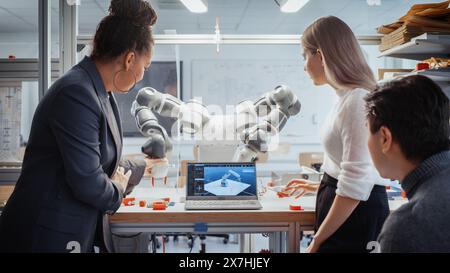 Black Professor Analyse and Discuss Futuristic Robotic Arm with Two Diverse Young Specialists in Research Laboratory with Laptop. Engineer Helping Students. Computer Science Project Concept. Stock Photo