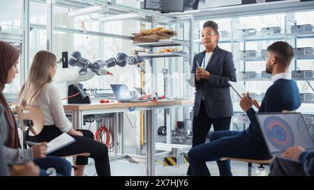 Corporate Meeting Room: Confident Black Female Engineer Talk with Intelligent Future Developers about Record Breakthrough in Robotics. Computer Science and Programming for Robotic Arm Concept. Stock Photo