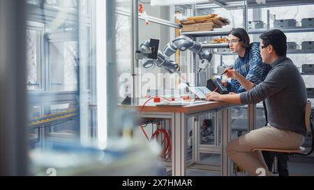 Two Diverse Developers Brainstorming and Coding on Laptop. Caucasian Male Press Button on Control Panel. Colleagues Building, Configuring and Testing Robots. Progressive Technologies Concept. Stock Photo