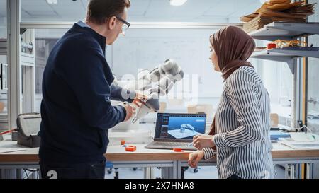 Promising Arabic Female Computer Scientist Asking Her Professor About Performance of Robotic Arm, While Standing Next To The Table in the Lab. Innovative Startup Company Concept. Stock Photo