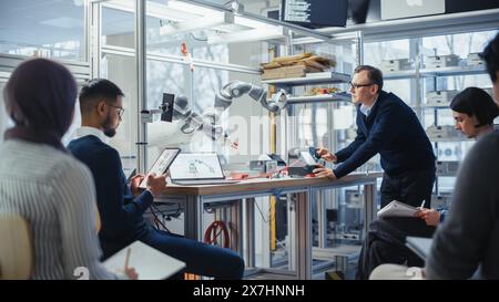 Diverse Computer Specialists Listen and Write While Senior Engineer Changing Position of Robotic Arm with Controller. Intellectual Youth in Modern Educational Environment Concept. Stock Photo