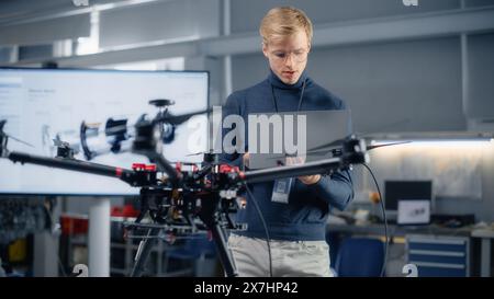 Young Male Developer Programming on Laptop Computer. Working on a New Drone Design in the Research Center Laboratory. People Creating Futuristic Unmanned Aerial Vehicle Concept. Stock Photo